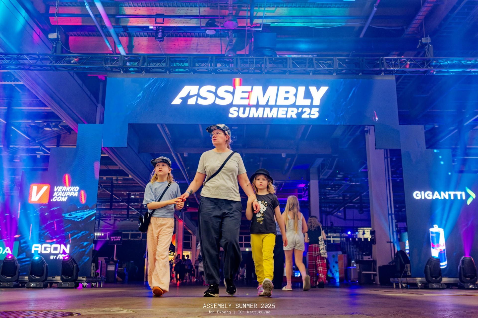 Family walking under the illuminated 'ASSEMBLY SUMMER '25' entrance arch