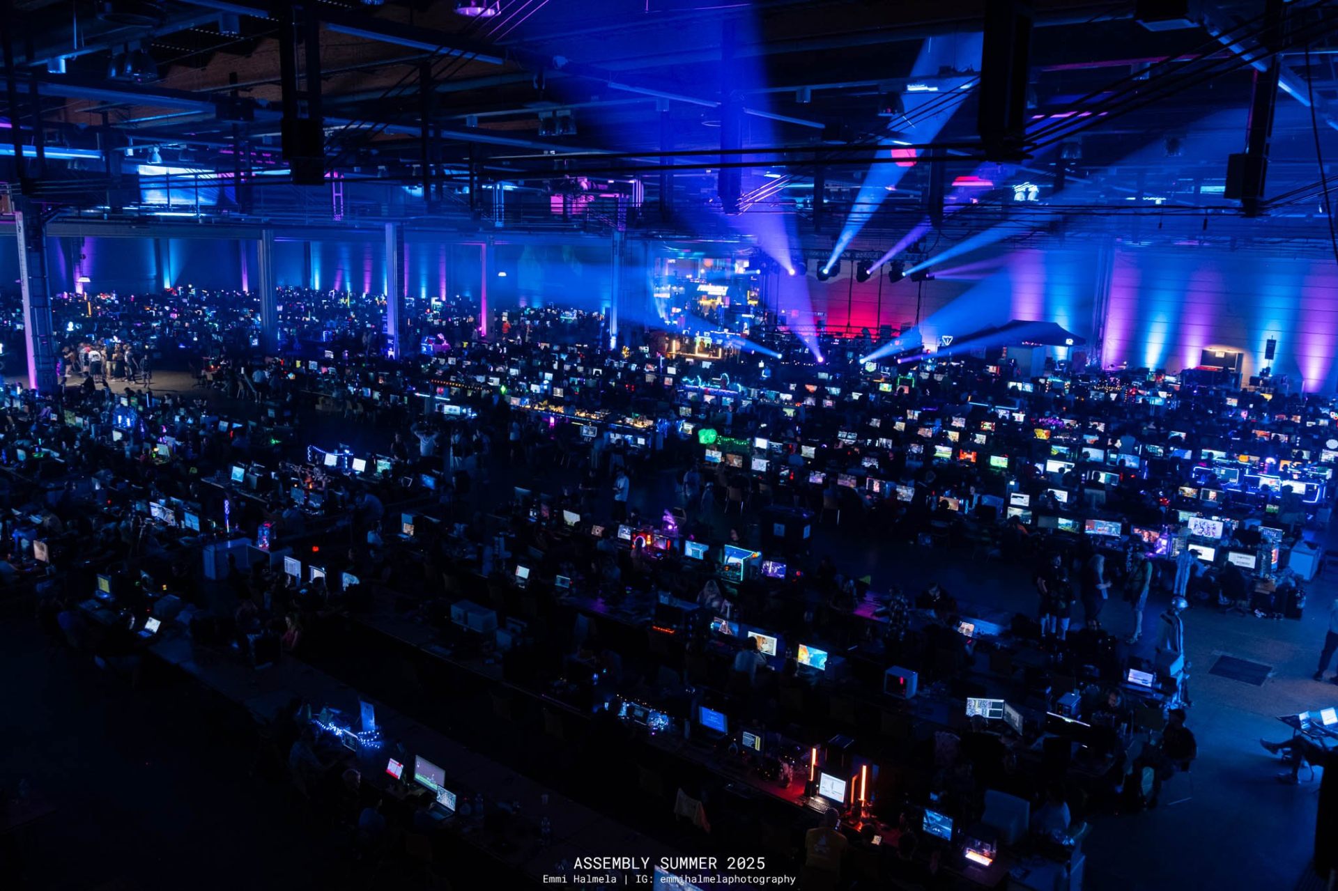 Wide view of the Assembly LAN hall lit by sweeping blue stage beams